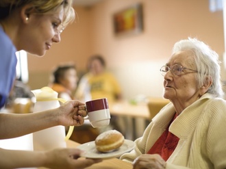 Altenheim, Pflegerin gibt Seniorin eine Tasse und Gebaeck