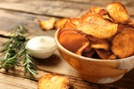 Delicious sweet potato chips in bowl, rosemary and sauce on table. Space for text