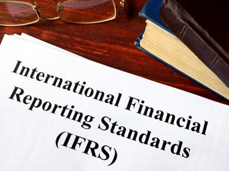 Dokument International Financial Reporting Standads auf Tisch mit Brille und Buch