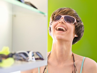 Junge Frau probiert in Boutique Sonnenbrille, lacht