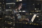 Frau sitzt in der Nacht im Bürogebäude und tippt am Laptop