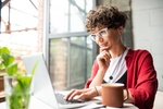 Busy young elegant woman in eyeglasses looking at laptop display while pressing keys of keypad durin