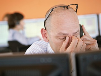 Gestresster Mann hinter PC, Brille hochgeschoben, fasst sich die Nase