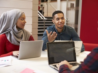 junge internationale Menschen diskutieren an Schreibtisch vor Laptops