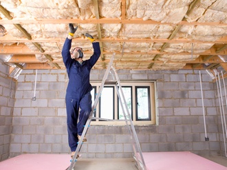 Man in coveralls and protective mask installing ceiling insulation