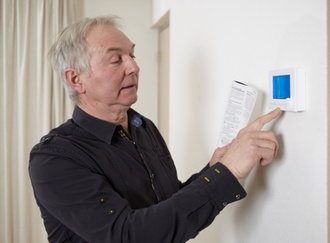 Alter Mann bedient mithilfe einer Bedienungsanleitung kleinen Bildschirm an der Wand