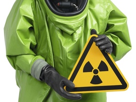 Mann im gruenen Schutzanzug haelt Radioaktiv-Schild