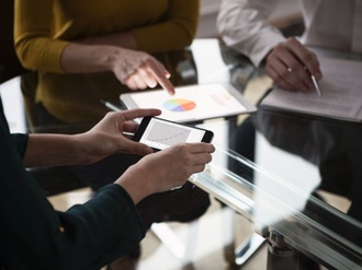 Mitarbeiter sitzen an Tisch und halten Grafiken auf Devices in der Hand