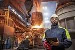 Stahlarbeiter mit Tablet in der Hand vor Hochofen