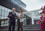 Mature businessman in suit talking to young business woman on stairs in front of office building